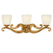 Hinkley Reese brushed-bronze vanity light with three pale cup shades and ornate scrolling arms.
