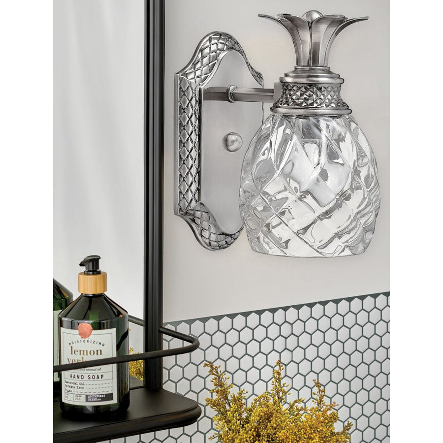 Hinkley Plantation sconce with clear glass below the leaf crown beside a bathroom mirror