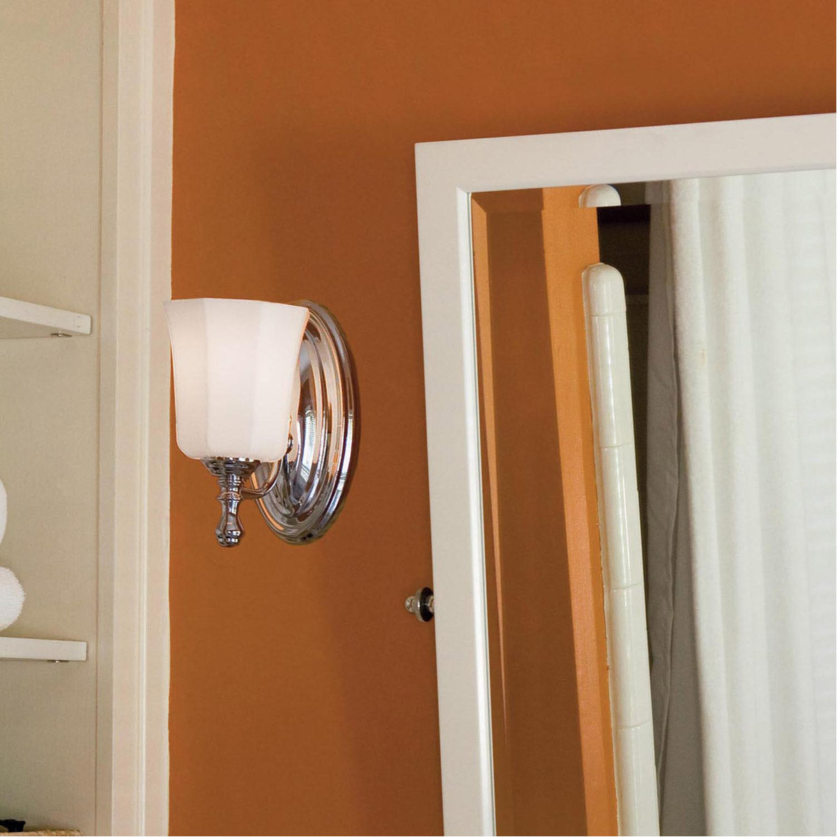 Hinkley Shelly sconce with an upward pale shade beside a mirror on an orange bathroom wall